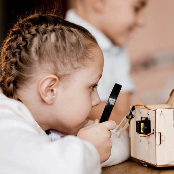 Child examining a wooden STEM project with a magnifying glass
